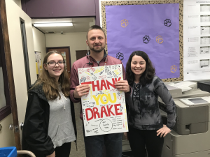 Travis Drake holding a sign that says, "Thank you Drake," while standing between two students (courtesy of Travis Drake)